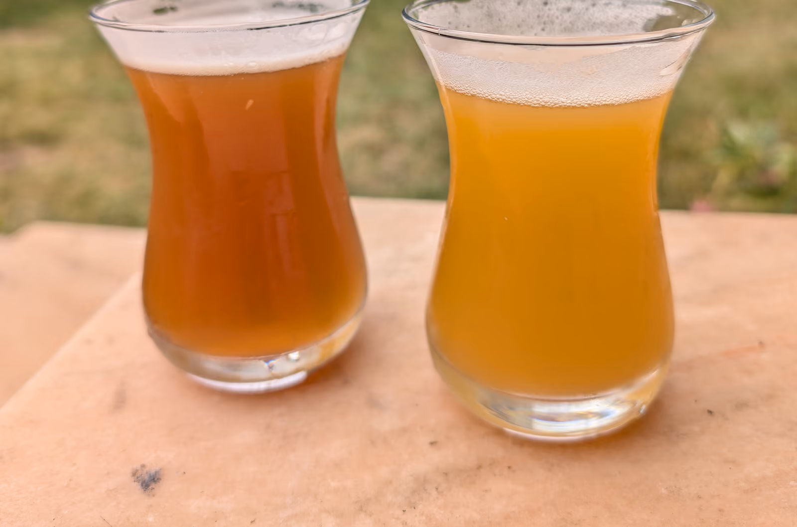 Deux verres de bière artisanale, l’un ambré et l’autre blond, posés sur une table en pierre.